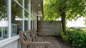 A wooden bench outside a building with large windows and a wooden wall.