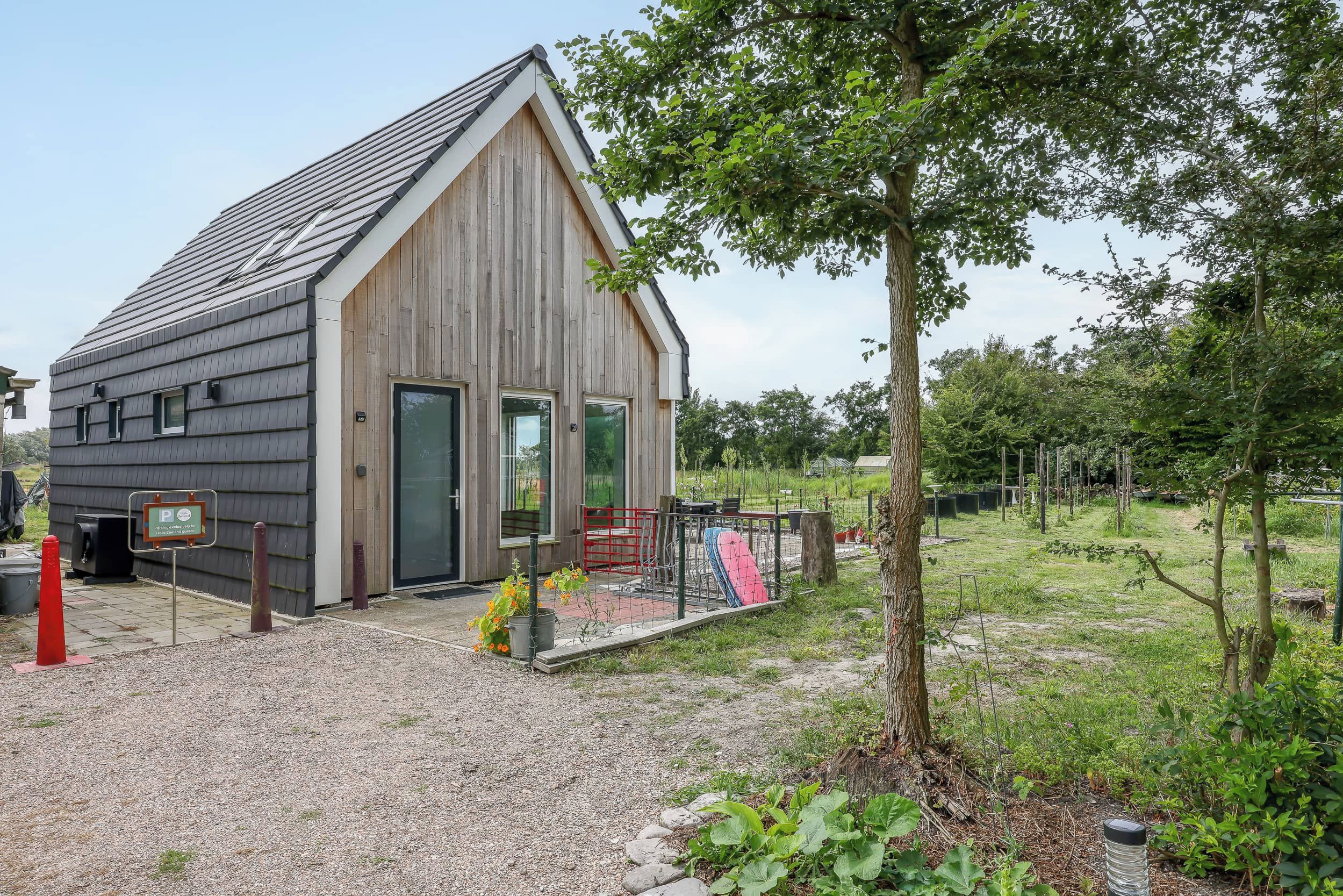 A wooden cabin with a sloped roof, a gravel driveway, and a fenced outdoor area with a tree.