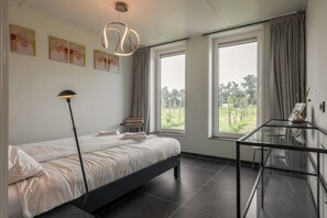 A modern bedroom with a bed, a glass table, and large windows with curtains.