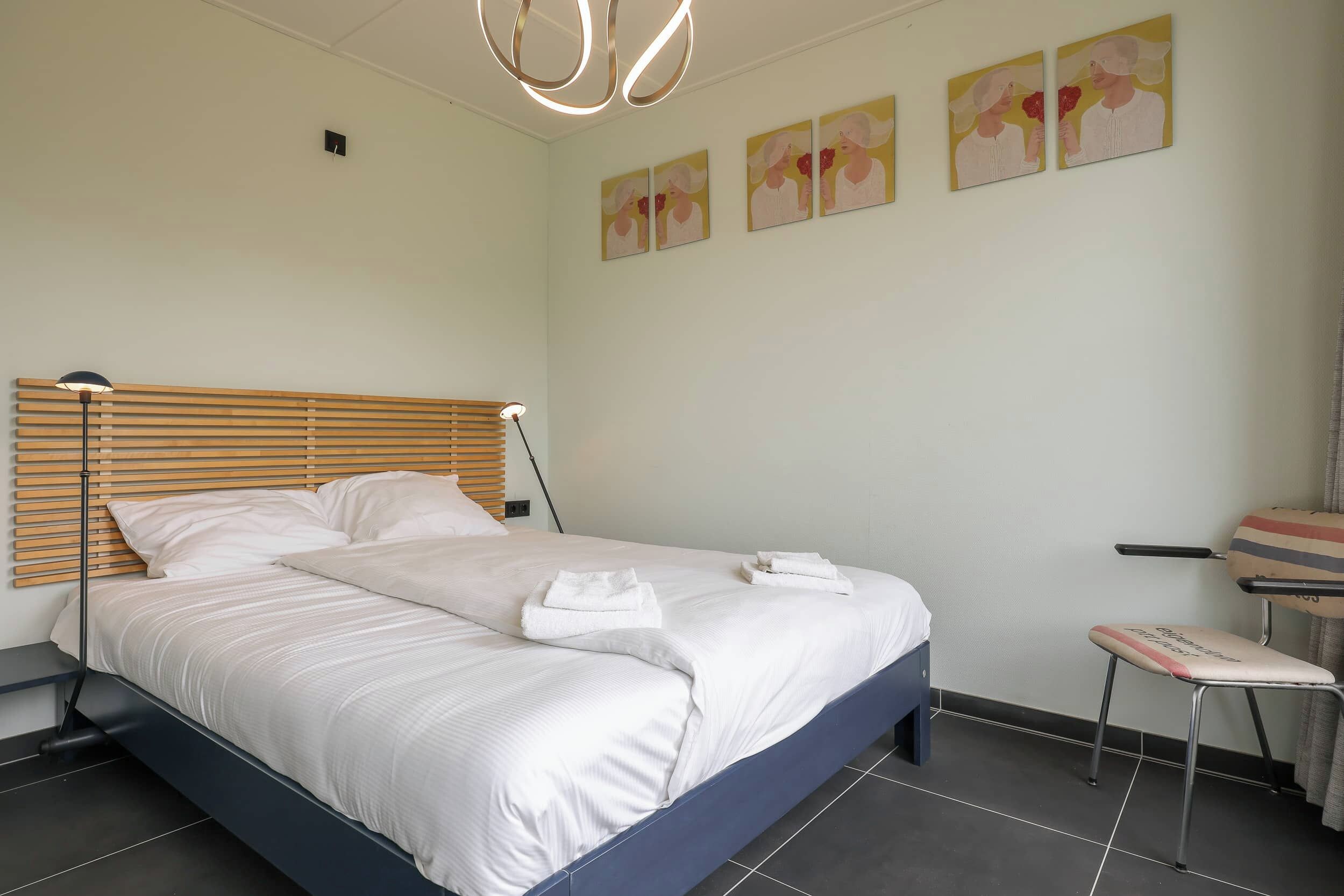 A neatly made bed with white linens and towels, a wooden headboard, and a small bedside table.