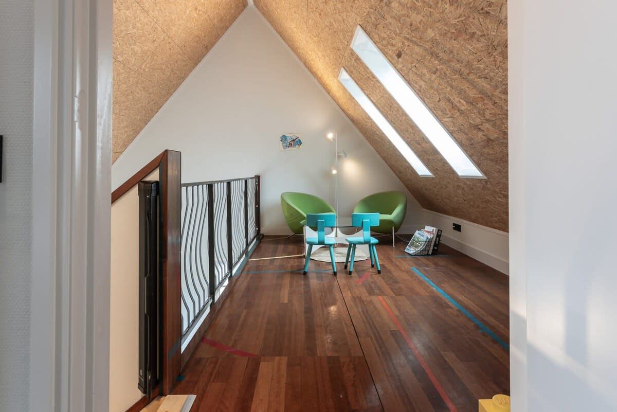 Un espai tipus loft amb sostre inclinat, sòl de fusta i una petita zona de seients amb dues cadires.
