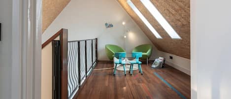 Una habitación tipo loft con techo inclinado, piso de madera y un pequeño rincón de estar con dos sillones.
