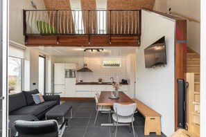 A modern kitchen with a dining area, a sofa, and a TV mounted on the wall. - Idyllic holiday home in Aagtekerke | Kalfhoeksepad 8 (Aagtekerke)