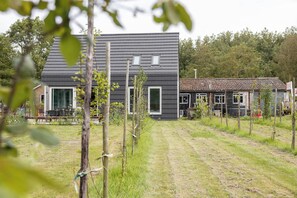 A modern house with a large front yard, a dining area with outdoor furniture, and a smaller adjacent building with a tiled roof. - Idyllic holiday home in Aagtekerke | Kalfhoeksepad 8 (Aagtekerke)