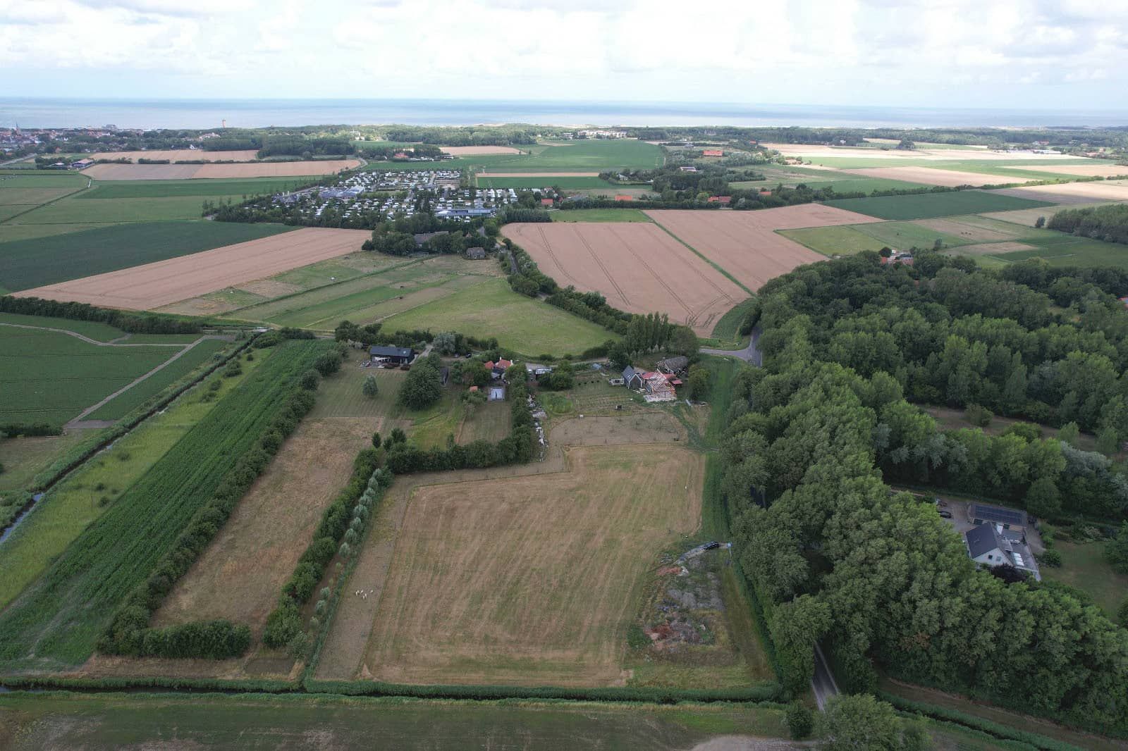 Vue aérienne d’une zone rurale avec des champs, un petit village et une étendue d’eau.