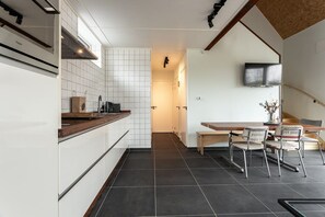 A modern kitchen with white cabinets, a dark tiled floor, and a wooden countertop. There is a bench and chairs in the dining area.