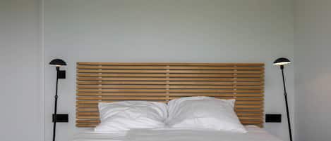 A neatly made bed with white linens and a wooden headboard.