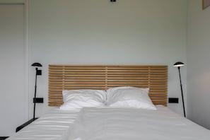 A neatly made bed with white linens and a wooden headboard.