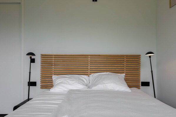 A neatly made bed with white linens and a wooden headboard.