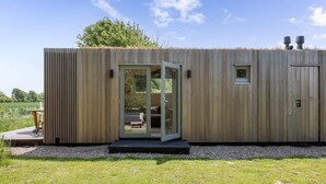 Una cabaña de madera moderna con puerta de vidrio corredera, un ventanal pequeño y un banco integrado en el exterior.