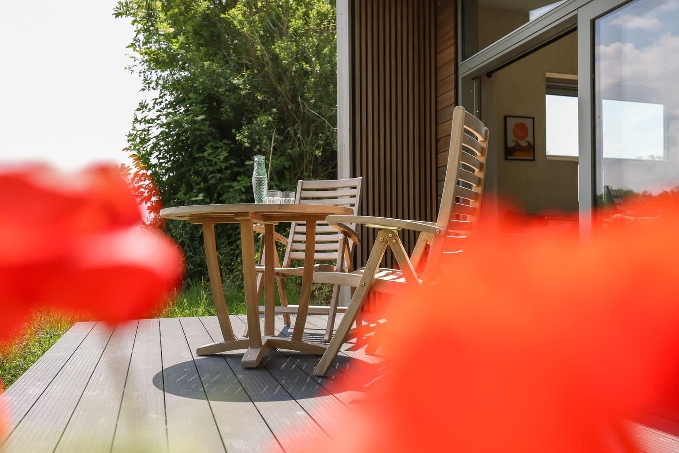 Una terraza de madera con una mesa y sillas, una botella de vidrio y un vaso sobre la mesa.