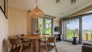 Un comedor moderno con una mesa redonda de madera, cuatro sillas, una lámpara colgante de fibras naturales y un televisor en la pared.
