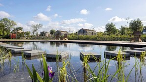 Un área de piscina tranquila al aire libre, con cielo despejado, rodeada de follaje y edificios modernos.