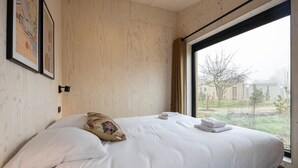A bedroom with a large bed, a window with a view of buildings, and a wooden wall.