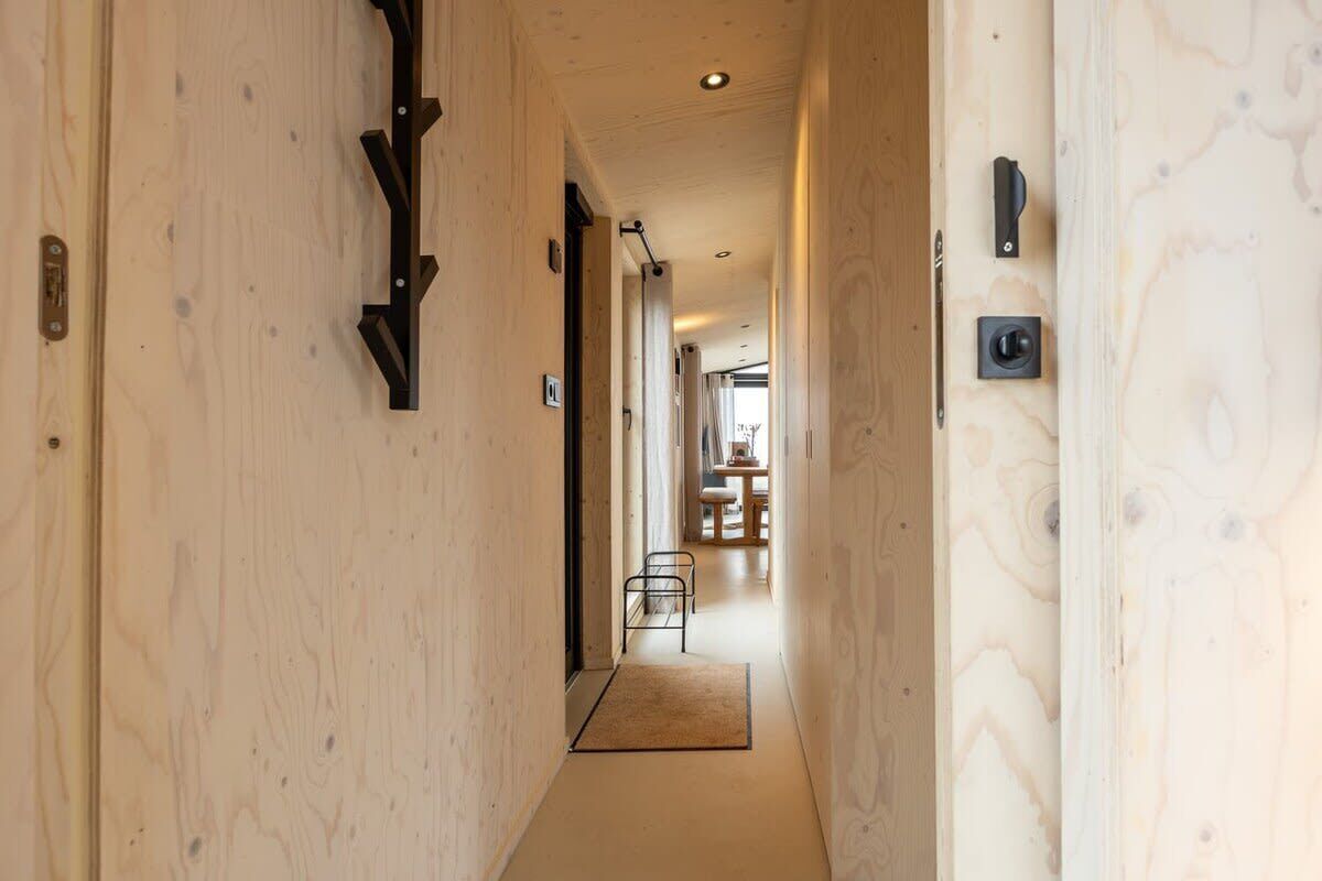Un pasillo estrecho con paredes de madera, una pequeña zona de estar al final y una puerta con pomo.