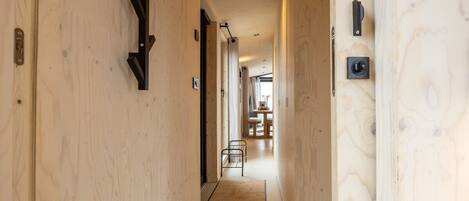 Un pasillo estrecho con paredes de madera, una pequeña zona de estar al final y una puerta con pomo.