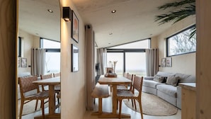 A modern interior with a dining area, a sofa, and large windows.