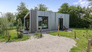 Ein modernes, eingeschossiges Haus mit einem großen Glasfenster, einer Schotterauffahrt und einer kleinen Gartenanlage.