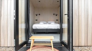 Ein modernes Schlafzimmer mit Glastür, Doppelbett und kleinem Holztisch.
