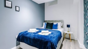 Une chambre à coucher moderne avec un lit, une literie bleue, une table de chevet avec une lampe et deux tableaux encadrés accrochés au mur.