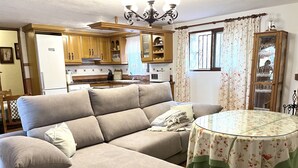A living room with a beige sectional sofa, a glass-top coffee table, and a dining table with a floral tablecloth. - EDMUNDO house with pool next to the beach (AN)