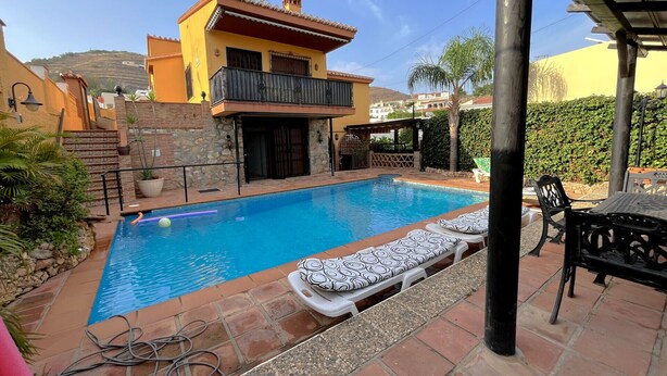 A swimming pool with lounge chairs, a stone wall, and a yellow building with a balcony. - EDMUNDO house with pool next to the beach (AN)
