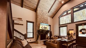 A spacious living room with a stone fireplace, a large window, and a cozy seating area.