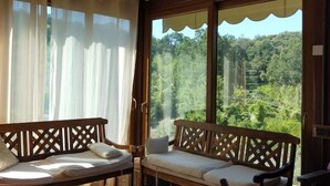 A balcony with two wooden benches, white cushions, and a view of a forested landscape. - Casa Foglia Verde - Immersa nel Parco (Liguria)