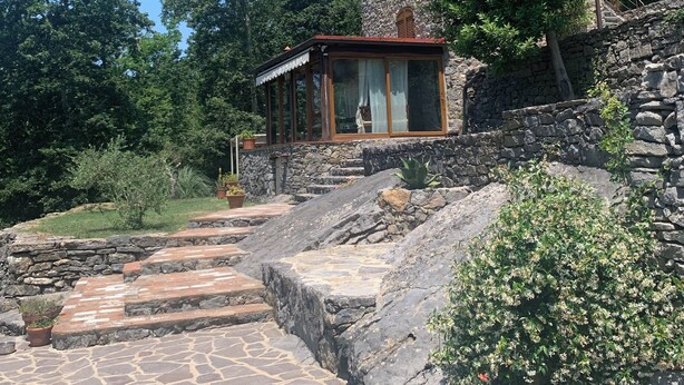 A stone building with a wooden deck and a stone staircase leading up to it. - Casa Foglia Verde - Immersa nel Parco (Liguria)