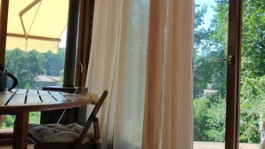 A room with a wooden table and chairs, a view of greenery outside, and a door with a view of trees. - Casa Foglia Verde - Immersa nel Parco (Liguria)