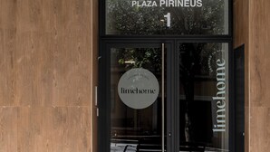A wooden bench outside a building with a sign reading "PLAZA PIRINEUS 1" and "limhome".