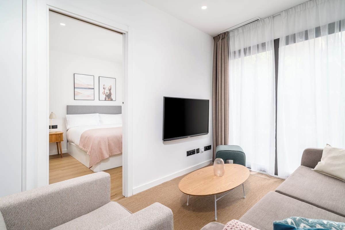 Ein modernes Hotelzimmer mit einem Bett, einem Fernseher, einem runden Holztisch und einer Couch.