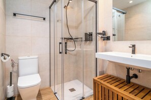 A modern bathroom with a glass-enclosed shower, a white toilet, and a wooden bench. - Limehome Barcelona Plaça Pirineus (L'Hospitalet de Llobregat)