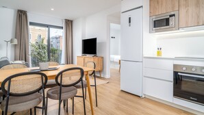 A modern kitchen with a built-in microwave, oven, and refrigerator. There is a dining area with a wooden table and chairs, and a television on a cabinet.