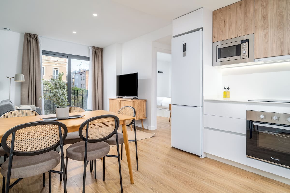 Eine moderne Küche mit integriertem Mikrowellenherd, Backofen und Kühlschrank. Es gibt einen Essbereich mit einem Holztisch und Stühlen, sowie ein Fernseher auf einem Schrank.