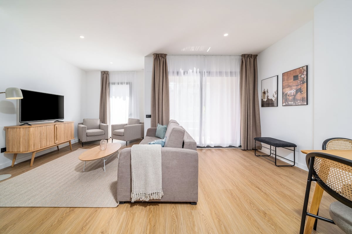 Ein modernes Wohnzimmer mit einer Couch, Sesseln, einem Fernseher und einem Essbereich.