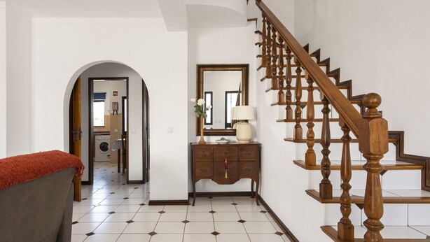Un couloir avec un escalier, un miroir, une commode et un coin buanderie.