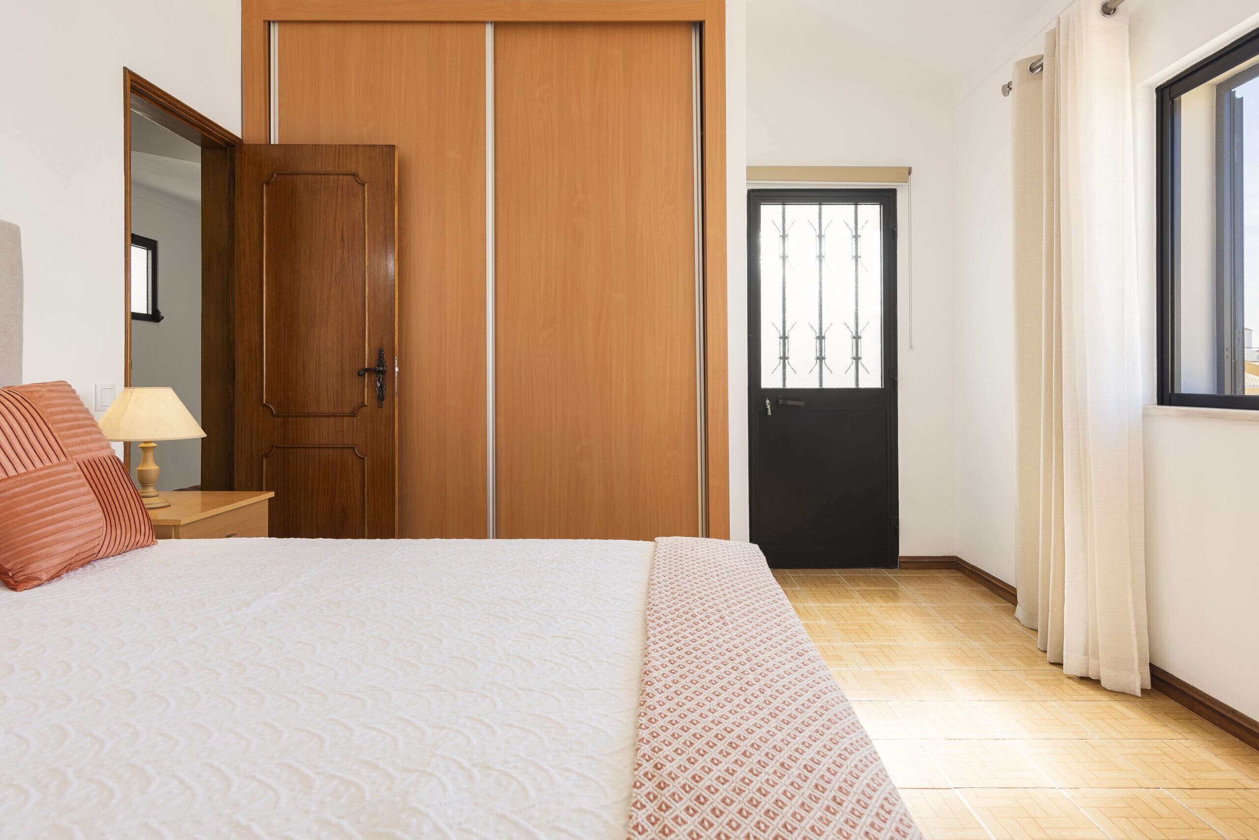 Une chambre à coucher avec un lit, une armoire en bois, une porte et une fenêtre.