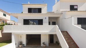 Une maison moderne à deux étages, dotée d’un patio couvert, d’un escalier et d’un petit jardin.