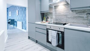 Een moderne keuken met grijze kastjes, een zwart fornuis en een betegelde achterwand.