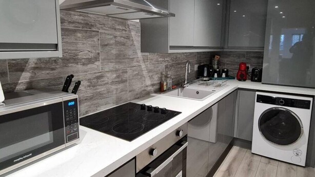 Een moderne keuken met een ingebouwde magnetron, kookplaat, spoelbak en vaatwasser.
