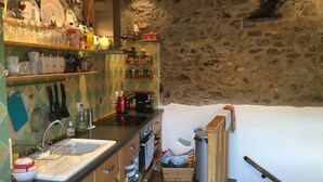 Eine rustikale Küche mit Steinwand, Holzregalen und verschiedenen Küchengeräten und -utensilien.