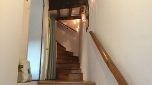 Eine Holztreppe mit Handlauf, die zu einem Raum mit einer Tür und einem Vorhang führt.