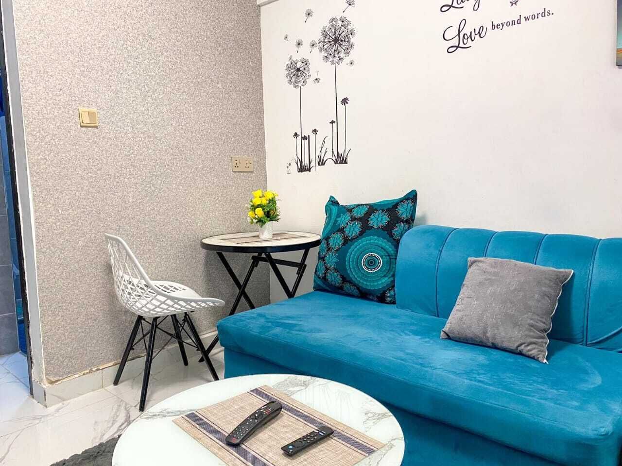 A room with a blue sofa, a white chair, a small round table with a vase of yellow flowers, and a wall with a dandelion illustration and the words "Love beyond words."