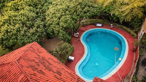 An aerial view of a swimming pool surrounded by lush greenery and a red-roofed building. - Hridey Retreat Resort (Ramnagar)