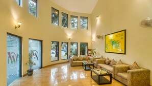A spacious lobby with high ceilings, large windows, and a modern sofa set. - Hridey Retreat Resort (Ramnagar)