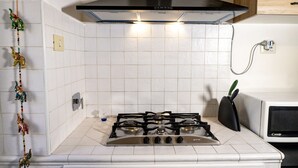 Cocina con estufa a gas, campana extractora negra, salpicadero de azulejos blancos y microondas.