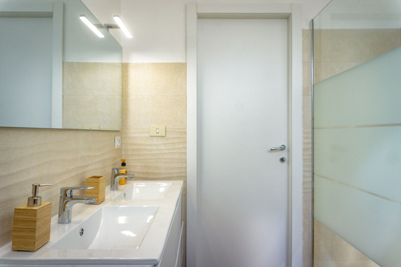 A modern bathroom with a white sink, mirror, and glass shower enclosure.