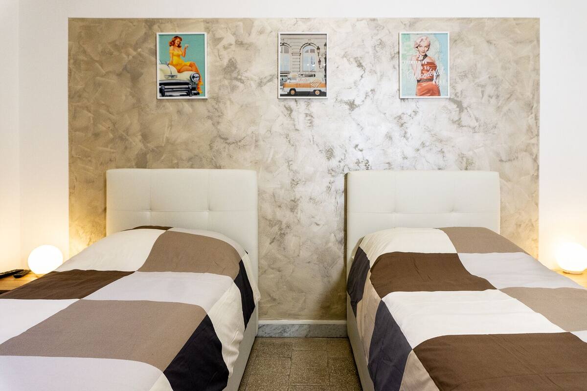 Two beds with a marble wall and three framed pictures.