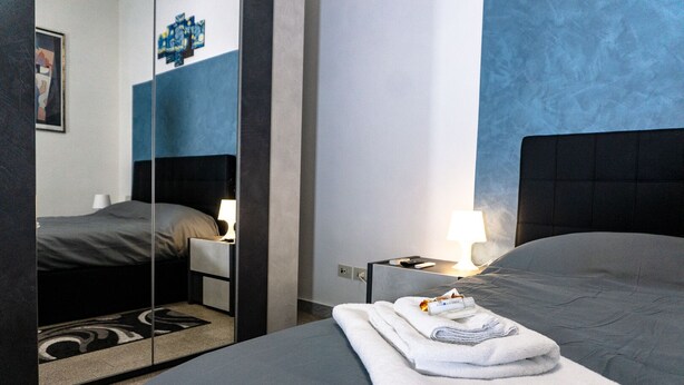 Habitación de hotel moderna con una cama grande, una mesita de noche con lámpara, un espejo y una toalla doblada con cuidado sobre la cama.